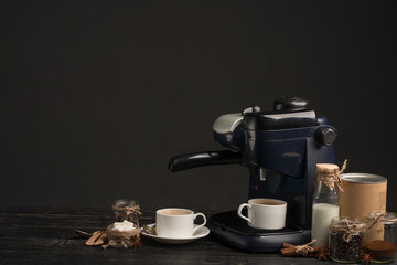 Coffee machine with a cup of coffee, with jars of coffee and milk on a dark background
