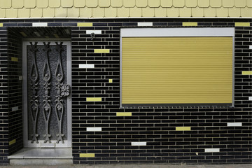 House facade in black brick with white and yellow touches, and a closed yellow shutter