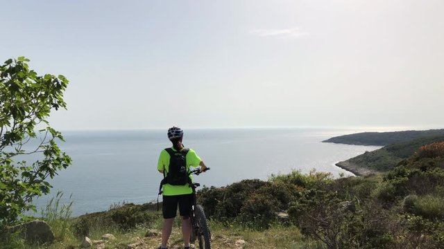 Woman on mountain bike looking at the ocean view on the top of a mountain