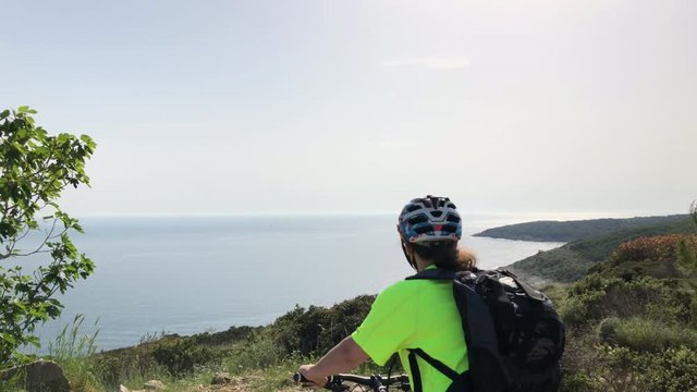 4K: Woman on bicycle on the top of the hill looking into the ocean