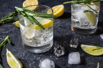 Poster Alcoholische drank gin tonic cocktail met citroen, rozemarijn en ijs op stenen tafel © voloshin311