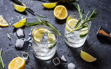 Alcoholic drink gin tonic cocktail with lemon, rosemary and ice on stone table