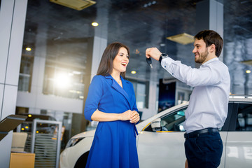 Delighted and admiring woman receiving keys from a new car from her husband standing near at avtosalon