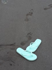 Mint green flip-flops on black sand