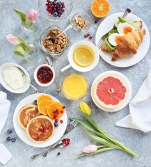 Breakfast set with pancakes, granola, croissant sandwich, grapefruit ,orange fresh and green tea. Table setting for festive easter breakfast. Overhead view
