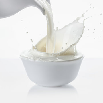 Pouring milk from jug in bowl on white background