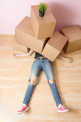 Photo of woman in jeans lying under cardboard boxes