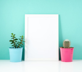 Blank white frame, plant cactus on white table against the blue wall. Mockup with copy space.