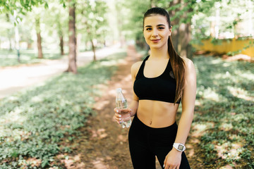 Young woman resting after jogging in park with water to drink