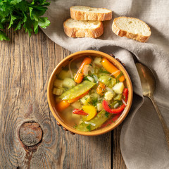 Bright spring vegetable dietary vegetarian soup. Top view, brown rustic wood background, linen napkin.
