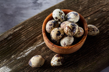 Wooden bowl filled with quail eggs on wooden board over white background, close-up, selective focus.