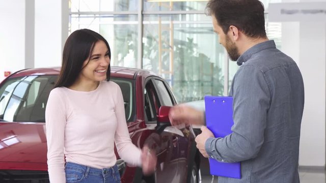 Happy beautiful young woman laughing joyfully receiving car keys to her new automobile. Cheerful female customer shaking hands with the salesman at the car dealership.