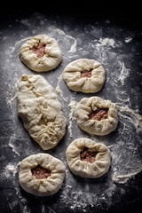 Pies with meat, potatoes and onions. The process of preparation on a black background covered with flour.