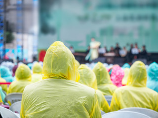 Crowded people in rain coat watching show in rains, rear view.