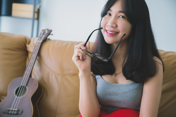 hobby music ukelele with beautiful asian woman in yellow shirt with happiness moment sing and play ukulel on bed white room background