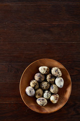 Fresh quail eggs in a wooden plate on a dark wooden background, top view, close-up