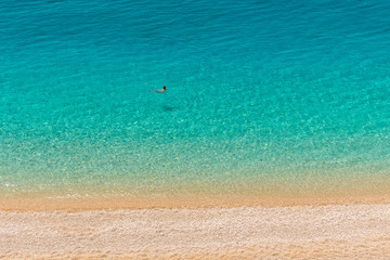A man is swimming into the crystal clear turquoise sea waters of a pebble beach. Porto Katsiki beach in Lefkada ionian island in Greece