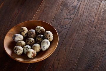 Fresh quail eggs in a wooden plate on a dark wooden background, top view, close-up