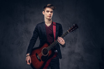 Stylish young musician with stylish hair in elegant clothes posing with a guitar in his hands. Isolated on a dark background.
