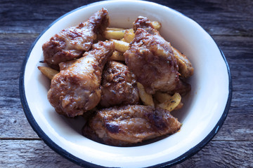 Appetizing chicken pieces and french fries with seasoning in a beautiful old bowl and on an old wooden background