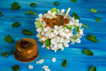 A cup of flower tea, decorated with apple blossoms and a beautiful chocolate cake, lies on a blue wooden table. Concept of spring drink.