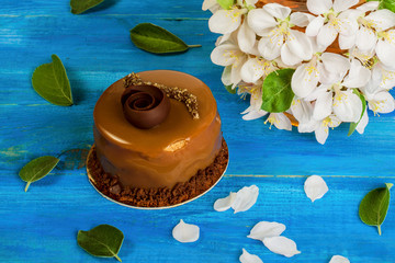 A cup of flower tea, decorated with apple blossoms and a beautiful chocolate cake, lies on a blue wooden table. Concept of spring drink.
