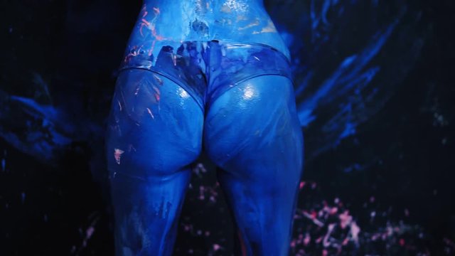 Sexy young woman shaking her blue butt, making twerk. Spreded with blue paint