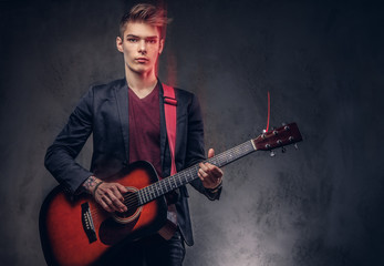 Obraz premium Stylish young musician with stylish hair in elegant clothes, playing on an acoustic guitar.