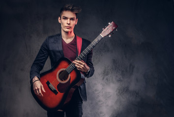 Obraz premium Stylish young musician with stylish hair in elegant clothes, playing on an acoustic guitar.