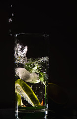 Splash of Cold fresh water with bubbles, lime, ice and mint in glass on black background