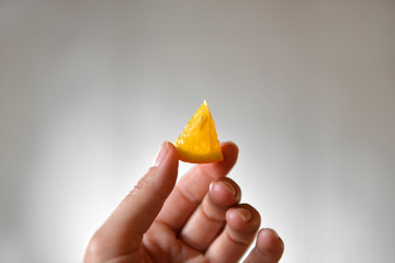 A small slice of orange in hands on a gray background. Orange in hand