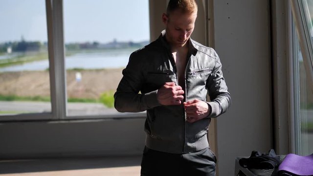 Young athletic man opening leather jacket on naked muscular pecs, abs and torso, undressing and taking it off. Tattoo says Don't stop dreaming, there's still time