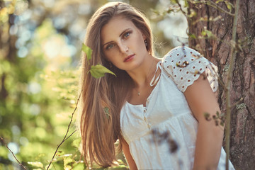 Naklejka premium Charming beautiful woman in a white dress posing in a green autumn forest.