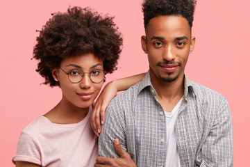 Cropped shot of lovely African American couple, embrace, stand close to each other: beautiful female in round eyewear leans at husband, enjoy free time together, have good relationship, understanding