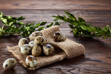 Quail eggs arranged in pyramid on a napkin with boxwood branches over a wooden table, close-up, selective focus.