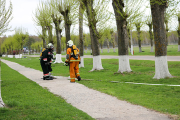Professional firefighters, rescuers in protective fireproof suits, helmets and gas masks flee...