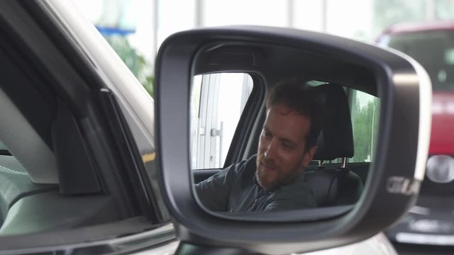 Close up shot of a car side mirror, mature man smiling happily sitting in his new automobile. Cheerful male customer enjoying his newly bought automobile. Buying cars, ownership concept.