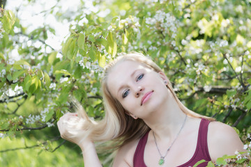 Smiling young blond woman is looking at the camera and with a leaning head is playing by her hand with her hair.