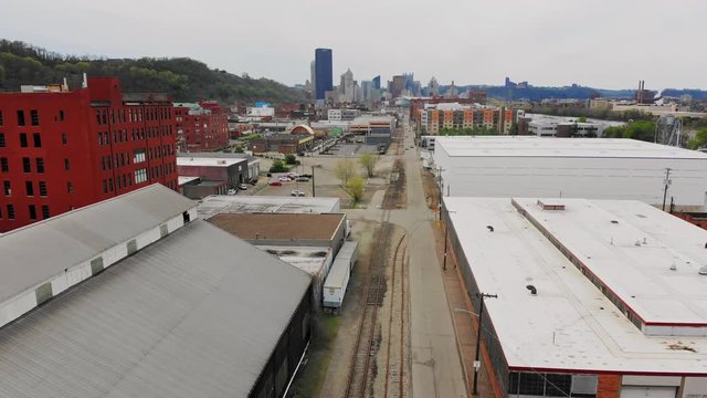 An aerial view of the various warehouses and industrial buildings in Pittsburgh's Strip District neighborhood with the city skyline in the far distance.  	