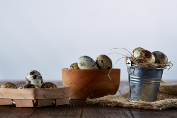 Rustic still life with quail eggs in bucket, box and bowl on a linen napkin over wooden background, selective focus