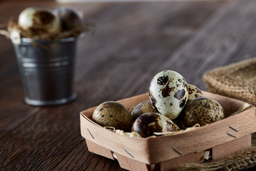 Rustic still life with quail eggs in bucket, box and bowl on a linen napkin over wooden background, selective focus