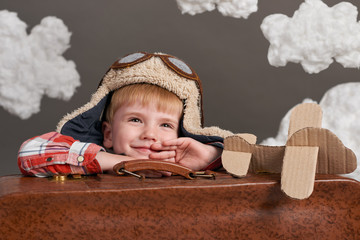 boy dressed as an airplane pilot sit between the clouds with old suitcase and playing with handmade plane
