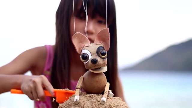 Little girl playing sand at the beach, happy with her puppy dog.
