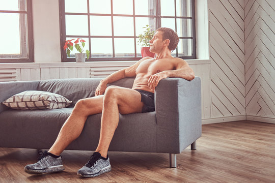 Handsome shirtless muscular man lying on the couch, resting after a hard workout at home.