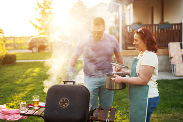 Cheerful couple is taking steamy meat off the grill and putting it in a pot on a beautiful day. © Dusan Petkovic