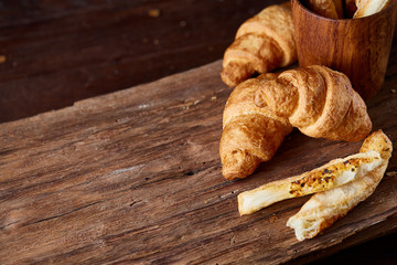 Puff pastries on piece of board over dark wooden table, close-up, selective focus, backlight.