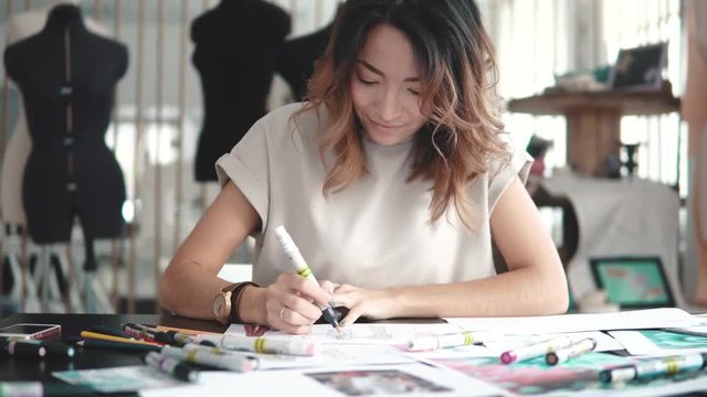 A young Asian woman working in a clothing store. A fashion designer makes outlines on paper.