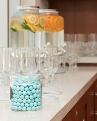 round blue candies and drinks set up in the background with bright light from a side displaying glass picther with tap containing refreshing lime orange and lemon with water for banquets and weddings