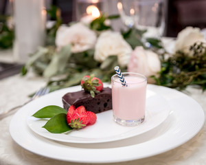 chocolate cake topped with strawberry and strawberry yogurt on a side with beautiful background of candles flowers and green leaves set in a luxury plate for a banquet 