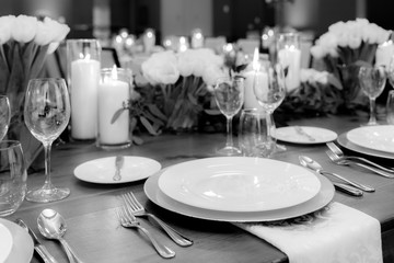 table set for banquet with silverware and glasses with elegant flowers white tulips and plants decoration as background also white candles lit up in black and white